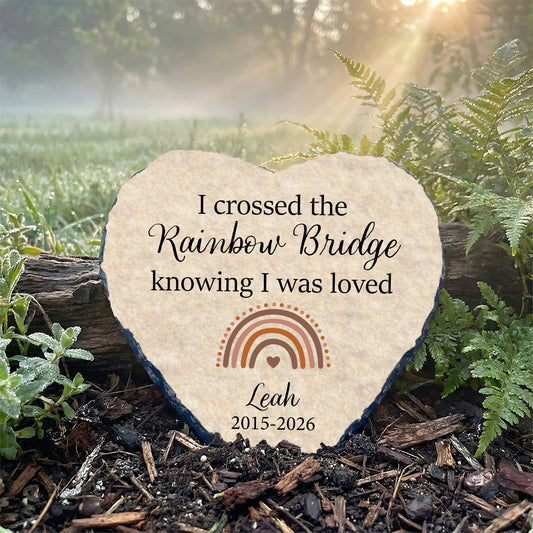 Heart-shaped stone with engraved text and rainbow design in a natural setting