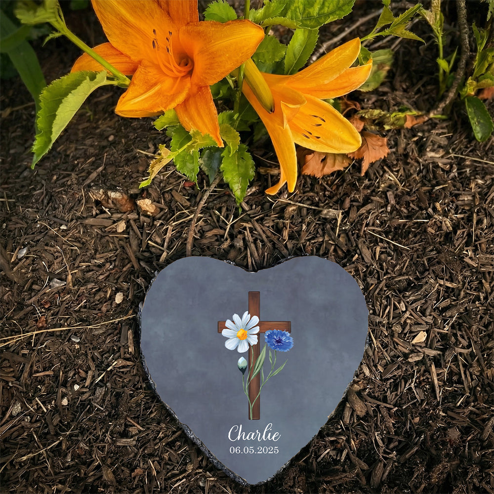 Heart-shaped memorial stone with cross and flowers on a grave with orange flowers in the background