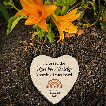 Heart-shaped pet memorial stone with engraved text on a bed of soil with orange flowers.