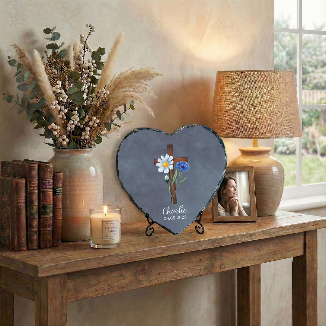 Heart-shaped slate with floral design and cross on a wooden table with decor items.