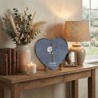 Heart-shaped slate with floral design and cross on a wooden table with decor items.