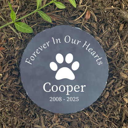 Memorial stone for a pet named Cooper with a paw print on a mulched surface.