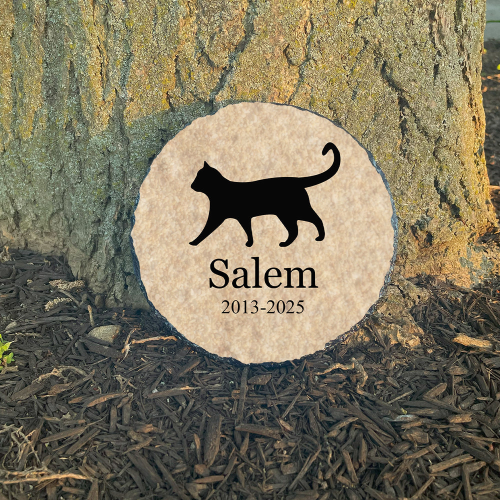 Memorial stone with a black cat silhouette and 'Salem' engraved, set against a tree trunk.