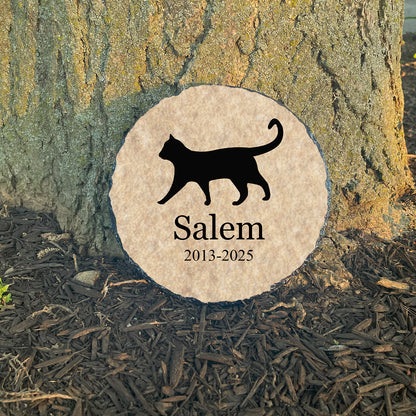 Memorial stone with a black cat silhouette and 'Salem' engraved, set against a tree trunk.