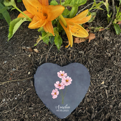 Heart-shaped stone with floral design and text on a garden bed with orange flowers.