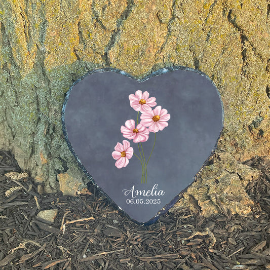 Personalized baby girl memorial stone at sunlit tree base. Features pink cosmos flowers. Customized with name Amelia. Hopeful sympathy gift.