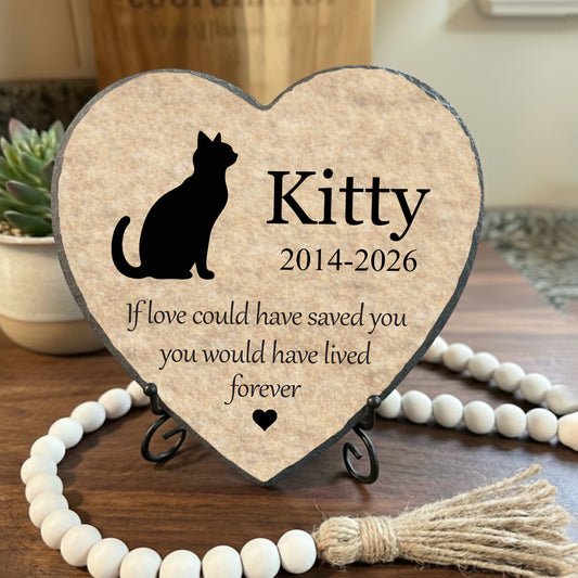 Heart-shaped wooden plaque with a cat silhouette and text on a stand, surrounded by decorative items.