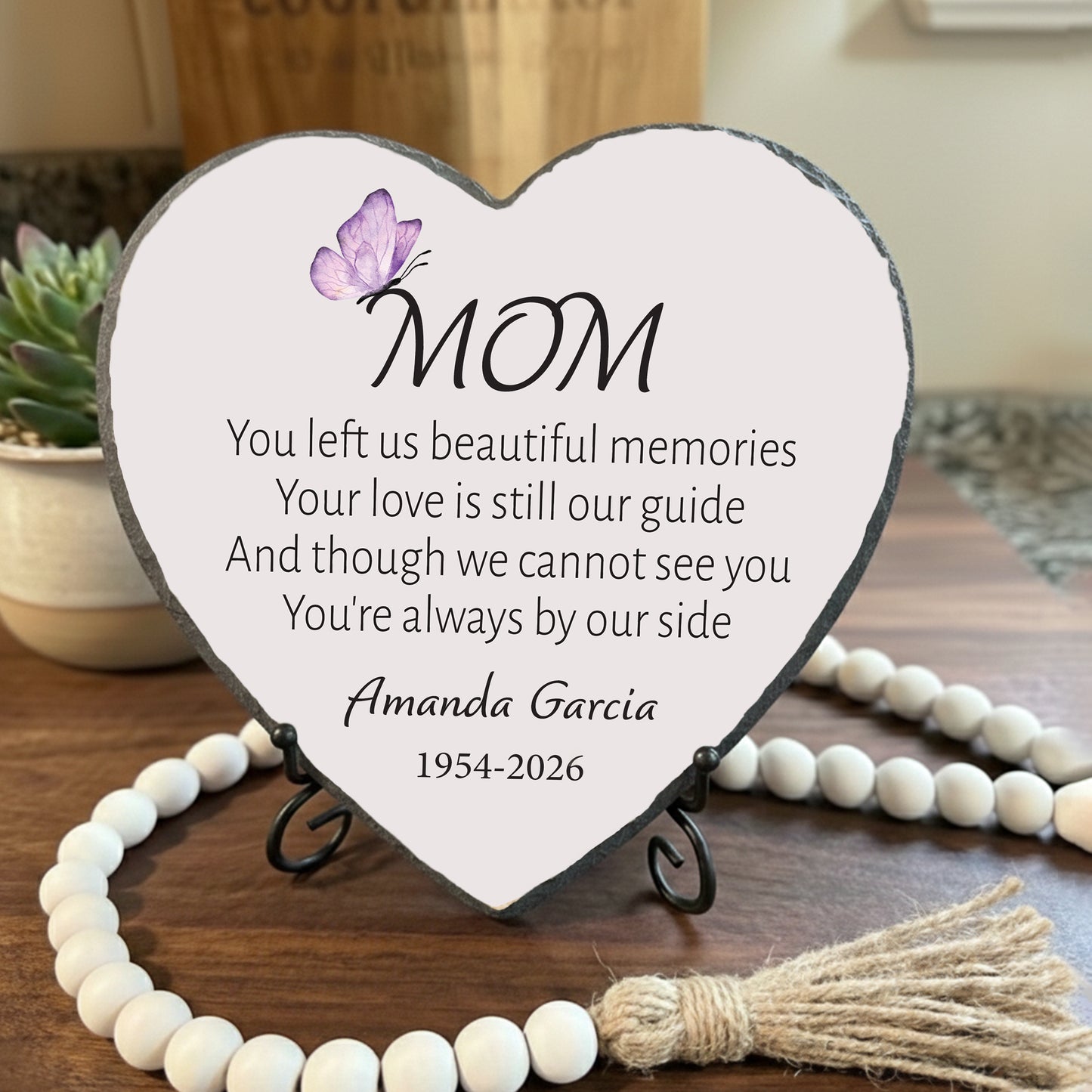 Heart-shaped plaque with a message for 'Mom' on a wooden surface with decorative elements.