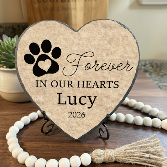 Heart-shaped plaque with paw print and text 'Forever In Our Hearts Lucy 2026' on a stand.
